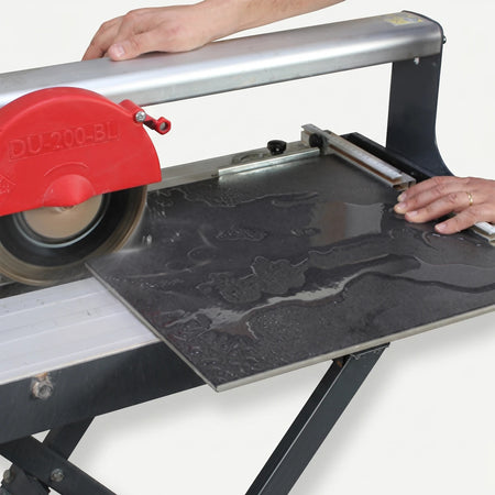 180mm Electric Wet Tile Cutter cutting a large dark grey tile, operated by hands from an overhead view.