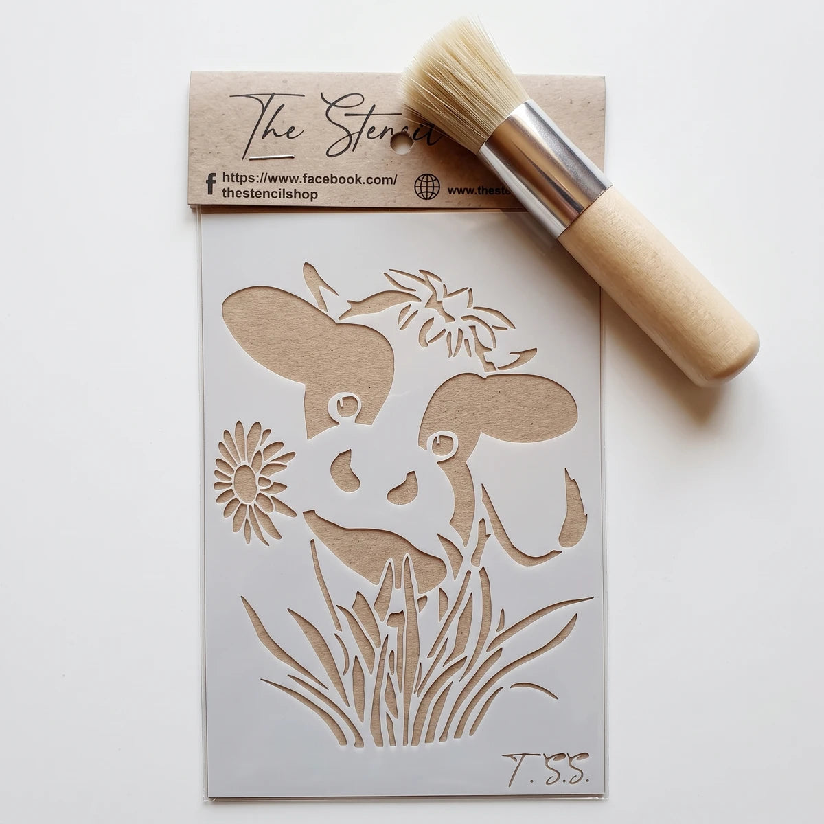 A rectangular stencil with a dog's face, flowers, and grass design, alongside a round stencil brush with a wooden handle.