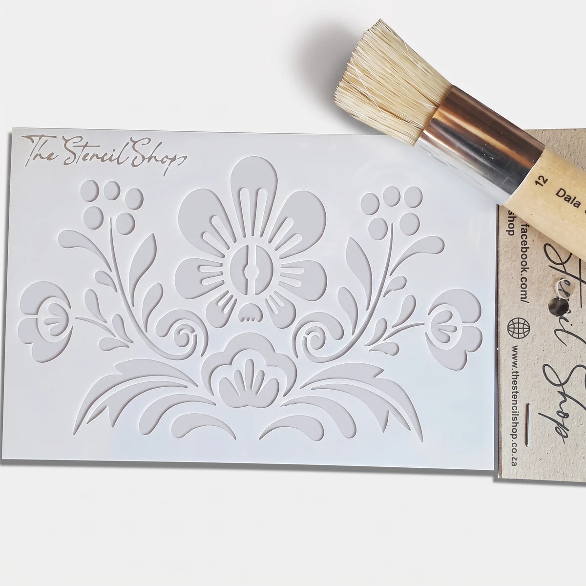 White plastic 2022-A6-9 Paint Stencil with a folk-art floral pattern, accompanied by a round stenciling brush, ready for
