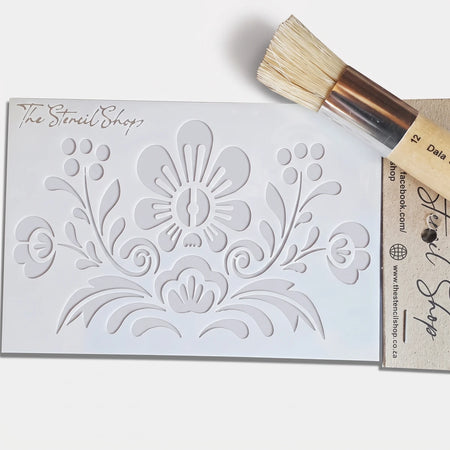 White plastic 2022-A6-9 Paint Stencil with a folk-art floral pattern, accompanied by a round stenciling brush, ready for