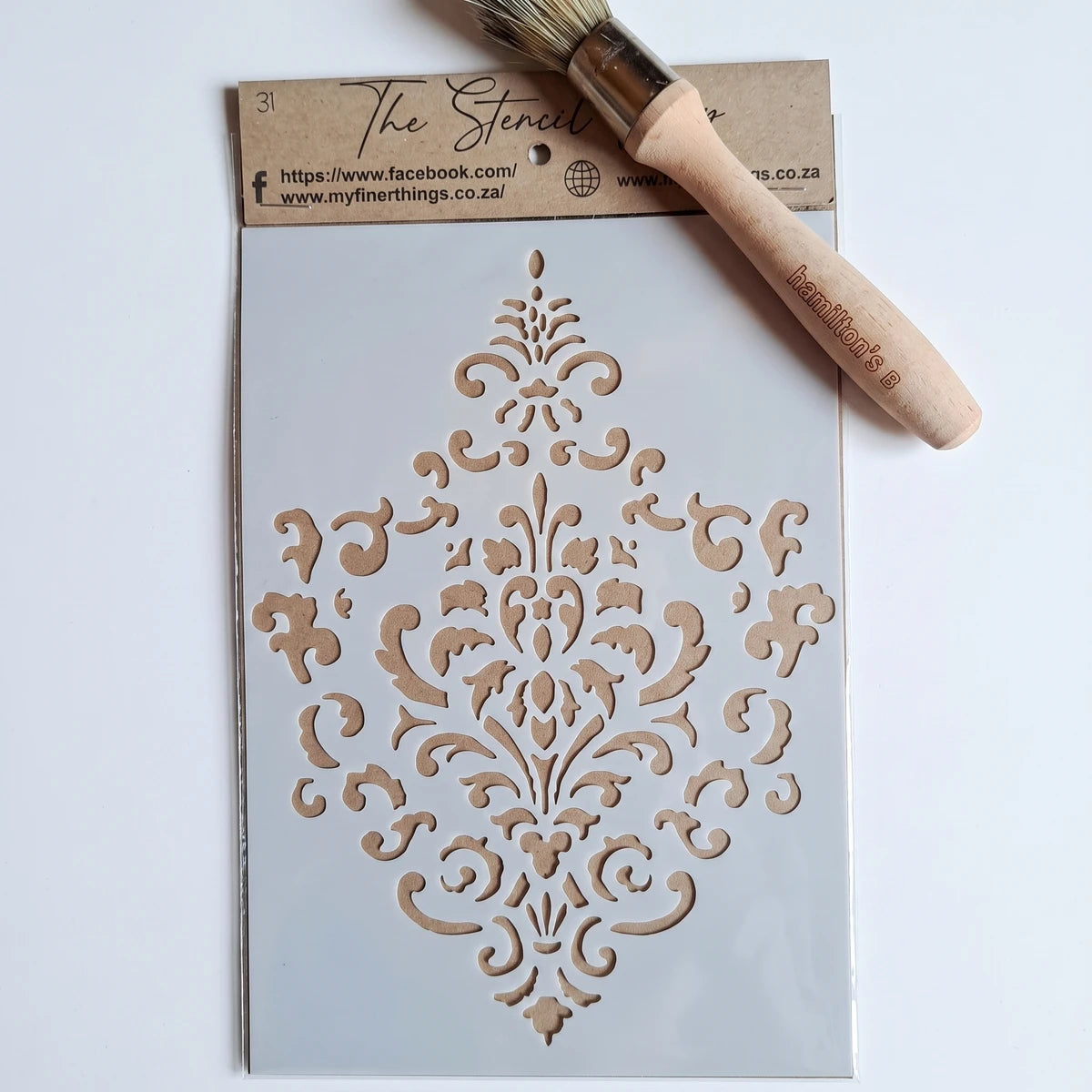 White A5-31 Stencil 51 with intricate damask pattern and a Hamilton's B paint stencil brush on a surface.