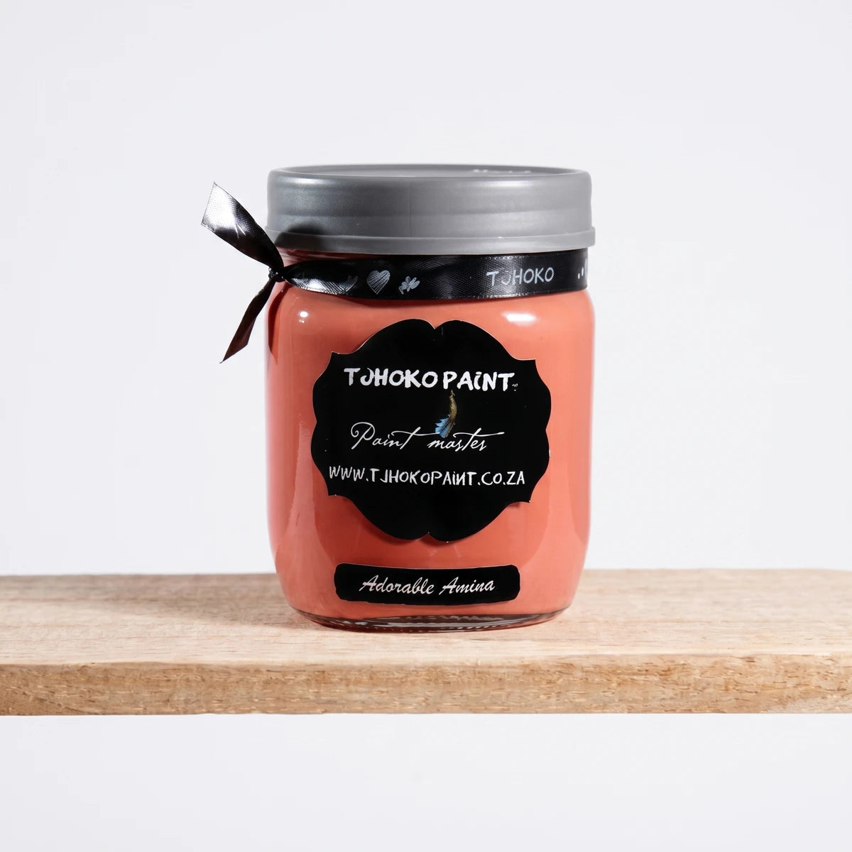 A single Adorable Amina 500ml paint jar, coral-colored with a gray lid and a black ribbon, displayed on a wooden shelf.
