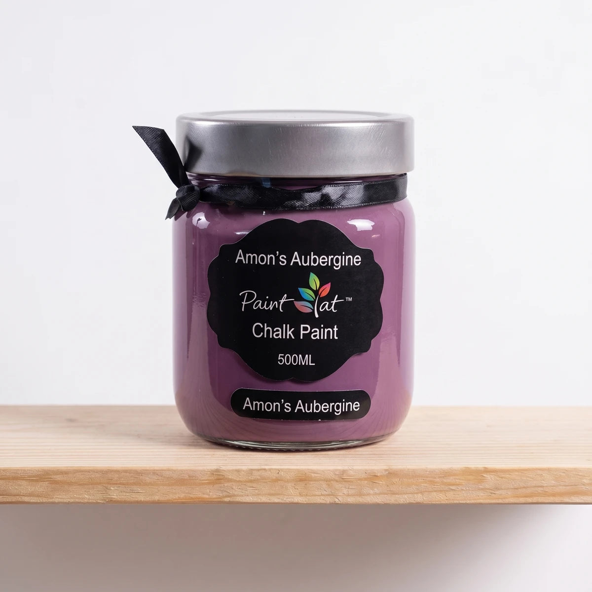 Amon's Aubergine 500ml Chalk Paint in a purple glass jar with a silver lid and black label, resting on a wooden shelf.