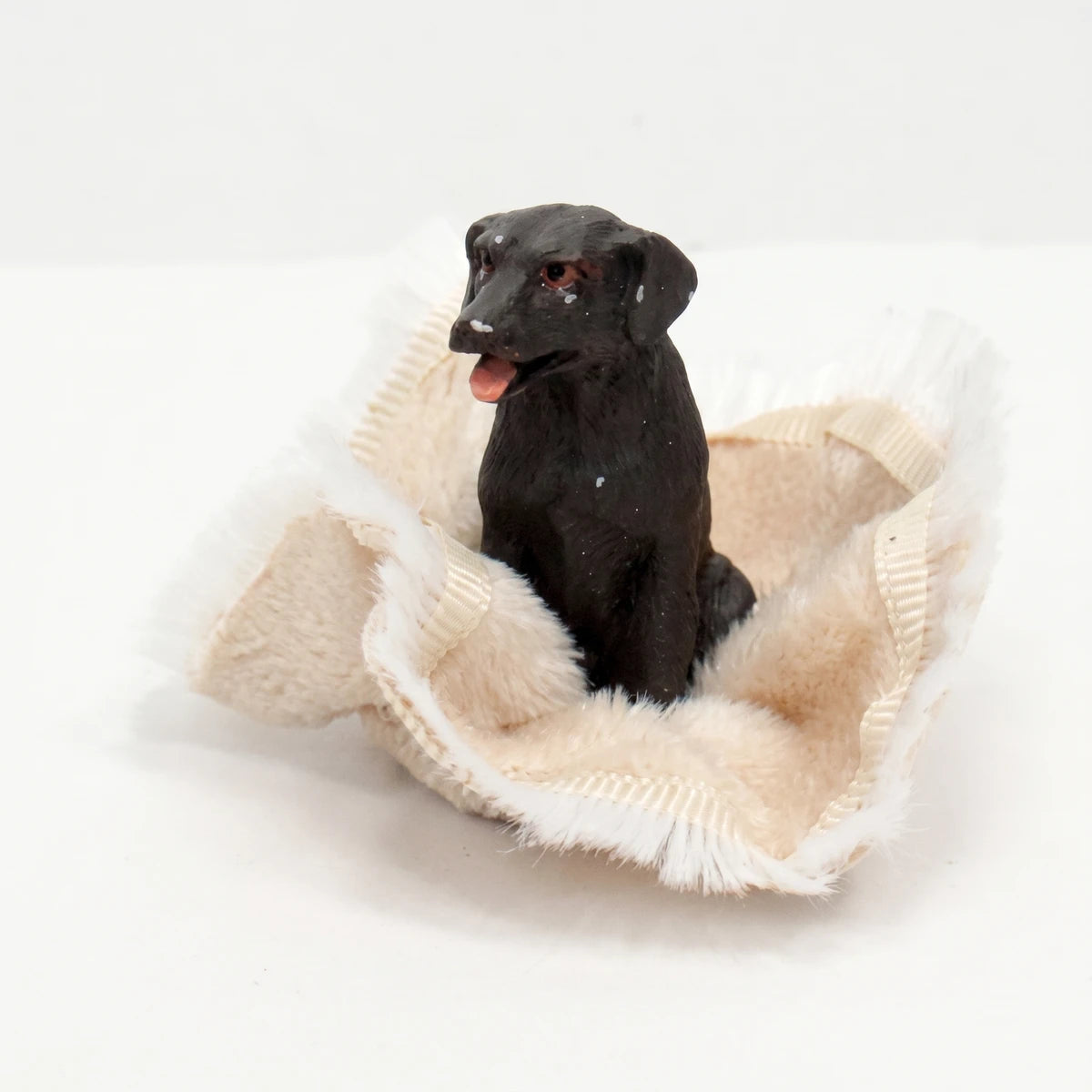 Black dog figurine sitting in a fluffy, light-colored pet bed. A miniature animal molding, 13cm x 13.5cm.
