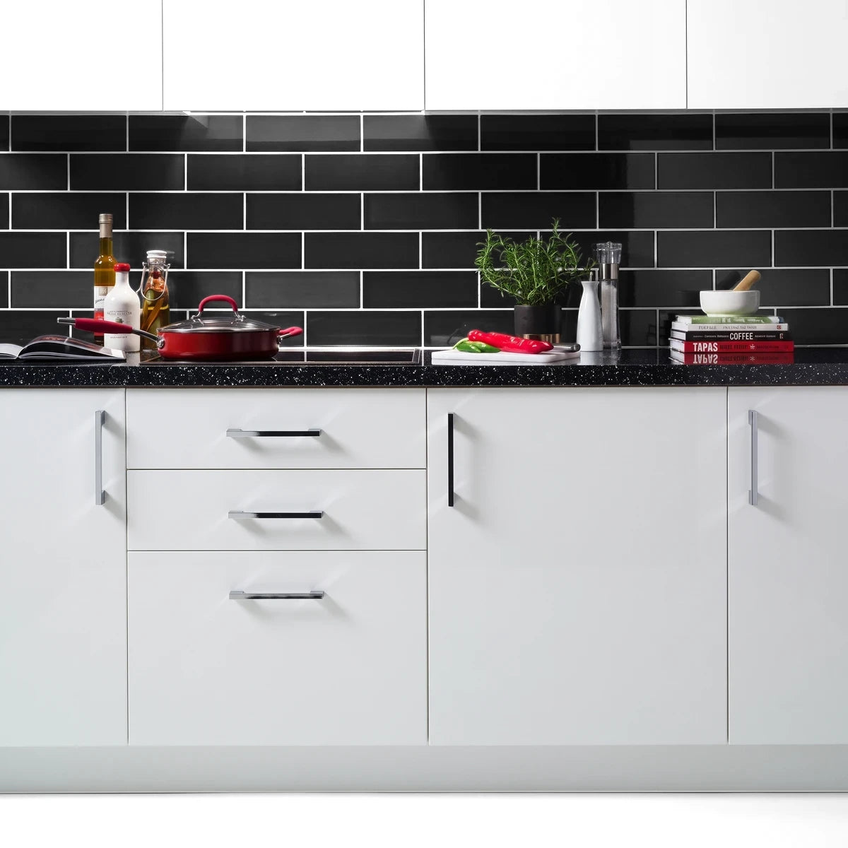 Modern kitchen with black gloss subway tiles backsplash, white cabinets, and black speckled countertop, styled with cooking