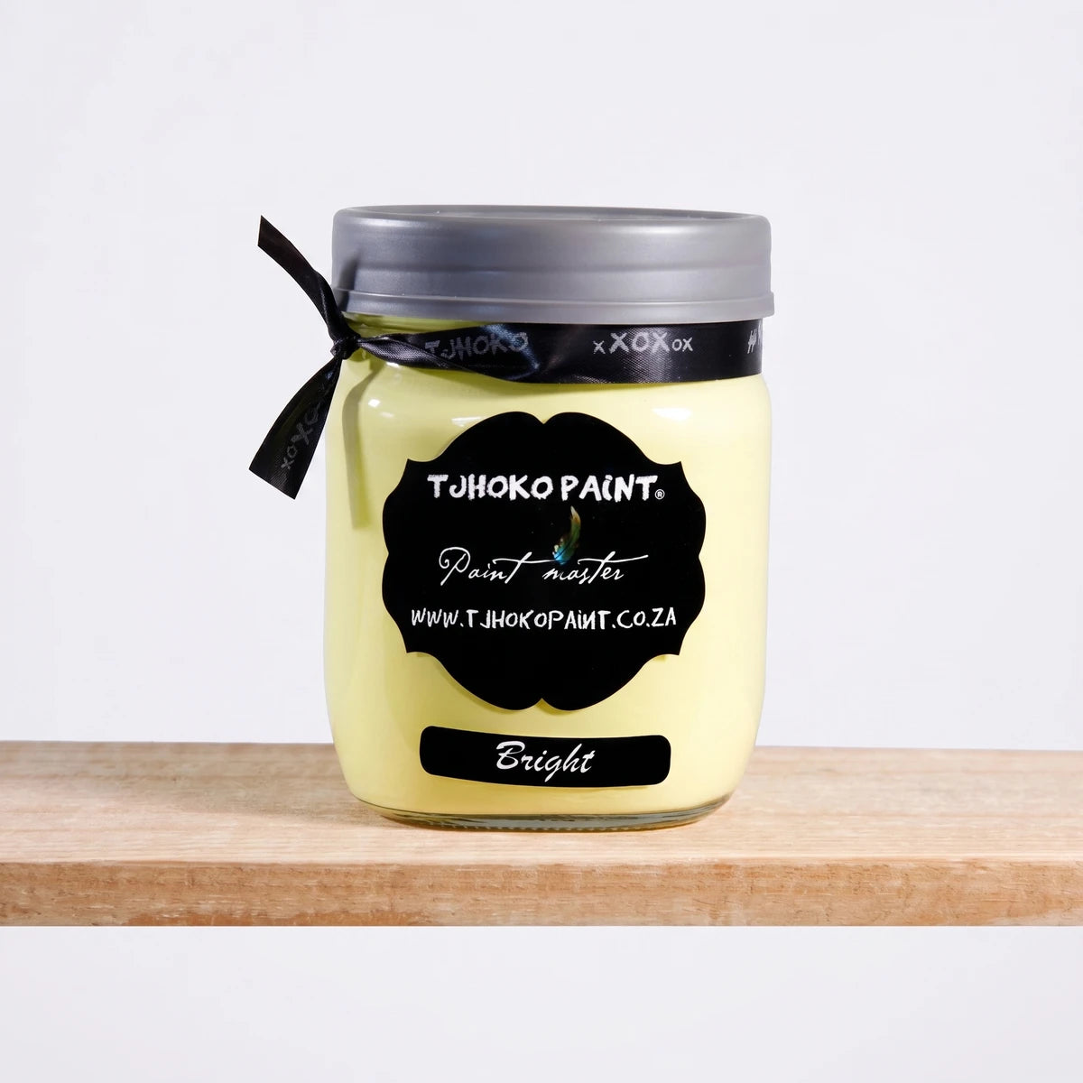 Bright 500ml Tjuhoko Chalk Paint in a clear glass jar with a black label, gray lid, and ribbon, resting on a wooden surface.