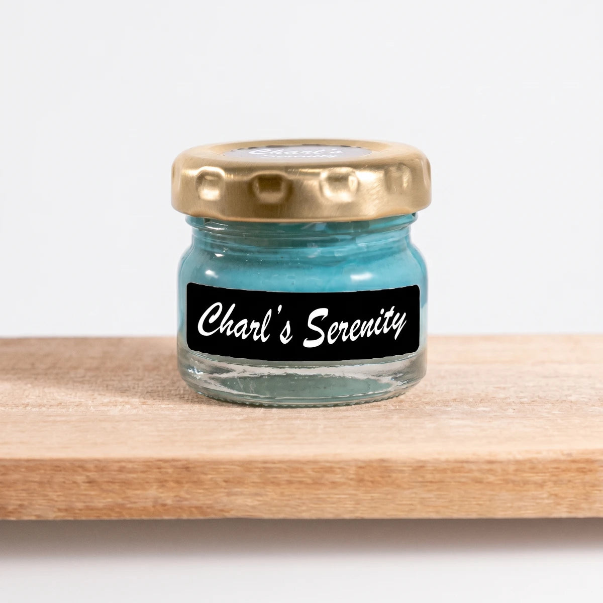 Small glass jar of Charles Serenity light blue paint with a gold lid and black label on a wooden shelf.