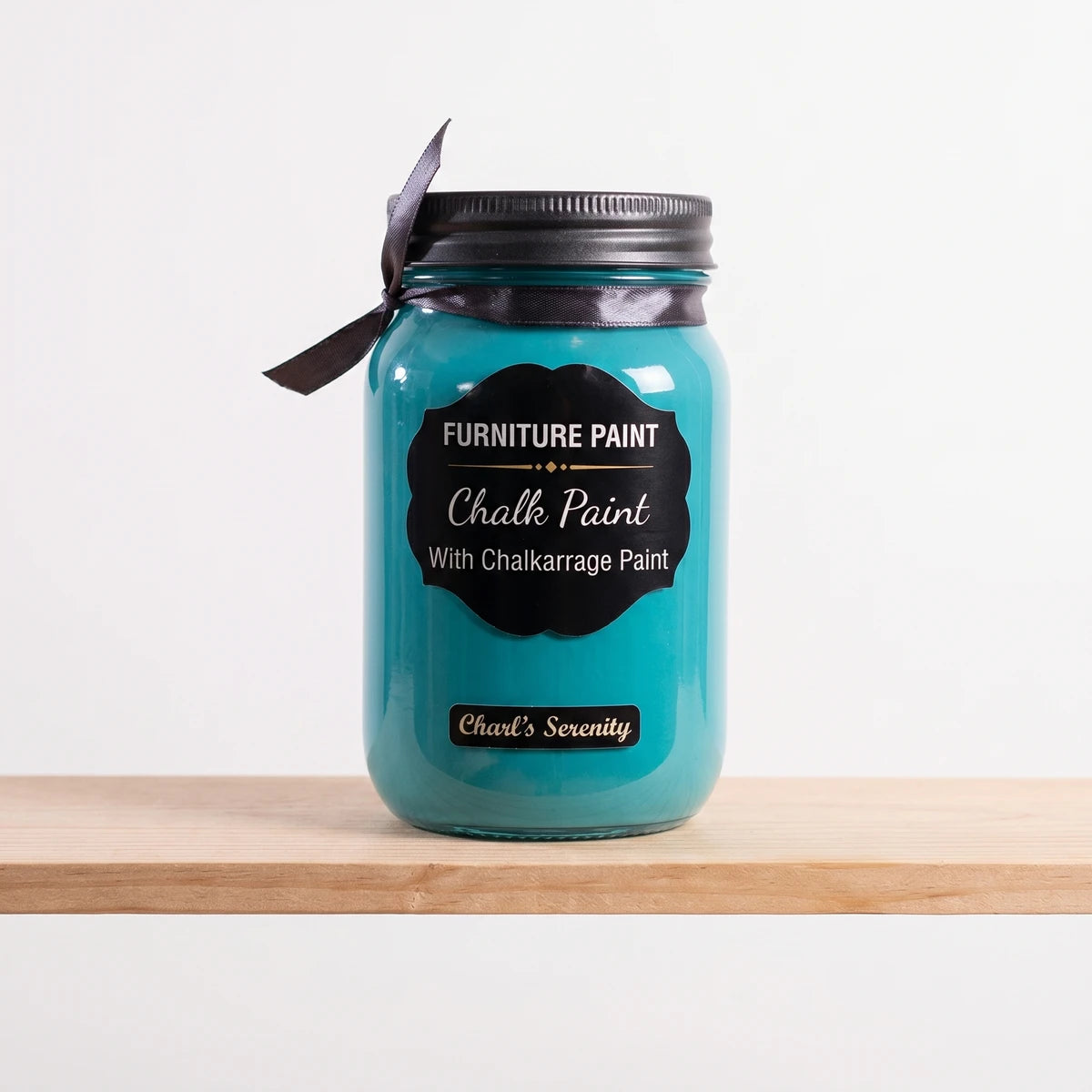 Charl's Serenity 250ml paint in teal, displayed in a glass jar with a black lid and ribbon, sitting on a wooden shelf.