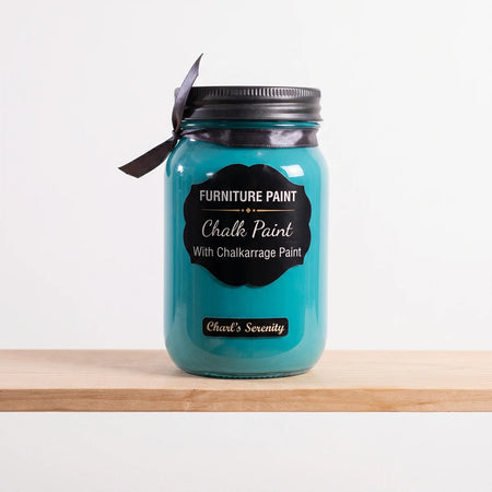 Charl's Serenity 250ml paint in teal, displayed in a glass jar with a black lid and ribbon, sitting on a wooden shelf.