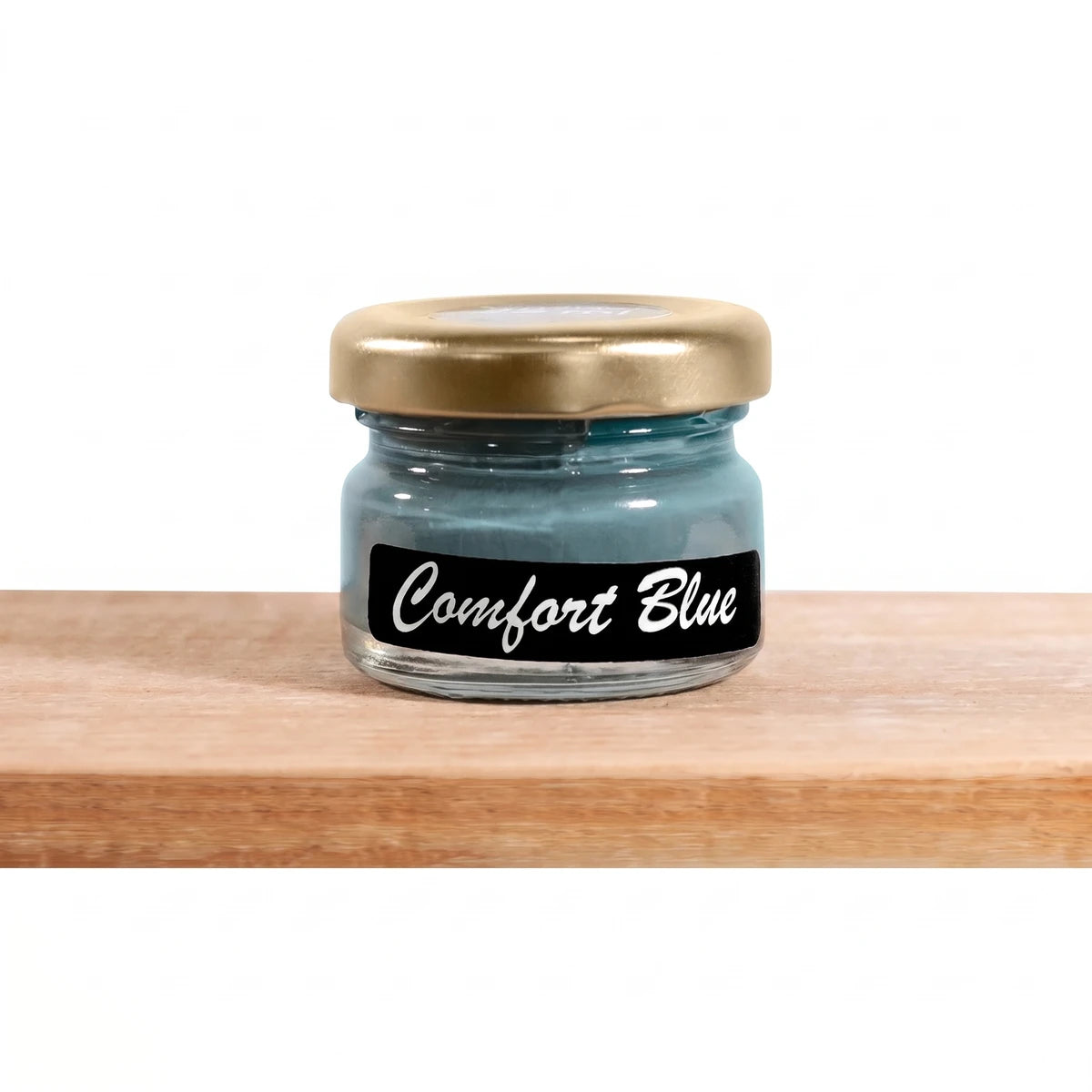 A small glass jar of Comfort's Blue 25ml Chalk Paint with a gold lid, resting on a light wooden shelf.