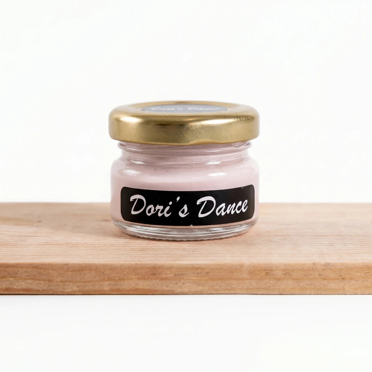 Small glass jar of Dori's Dance 25ml pink chalk paint with a gold lid and black label, resting on a wooden surface.