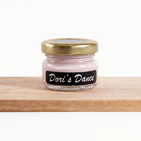 Small glass jar of Dori's Dance 25ml pink chalk paint with a gold lid and black label, resting on a wooden surface.