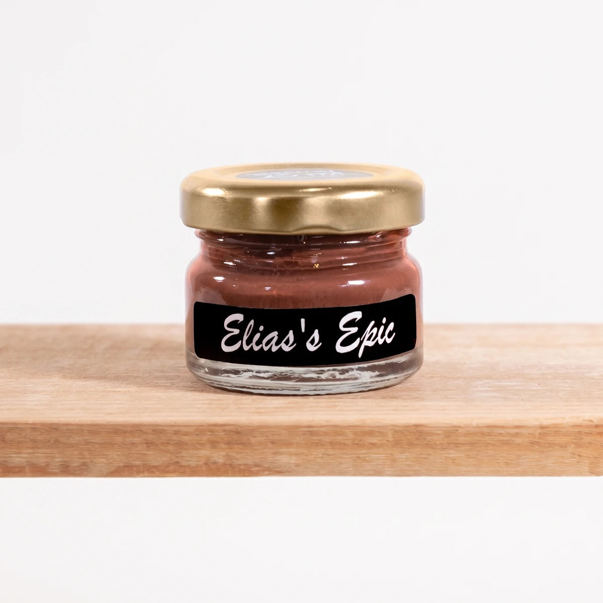 Elias' Epic 25ml chalk paint in a small glass jar with a gold lid, featuring a black label, displayed on a wooden shelf.