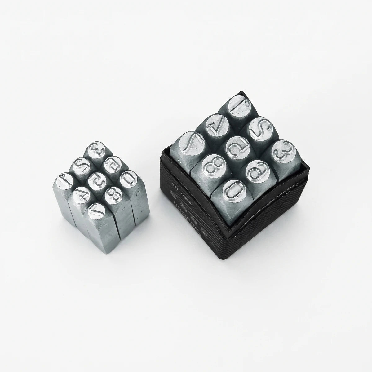 Two sets of gray metal number and symbol punch stamps, one loose and one in a black storage case, used for stamping.