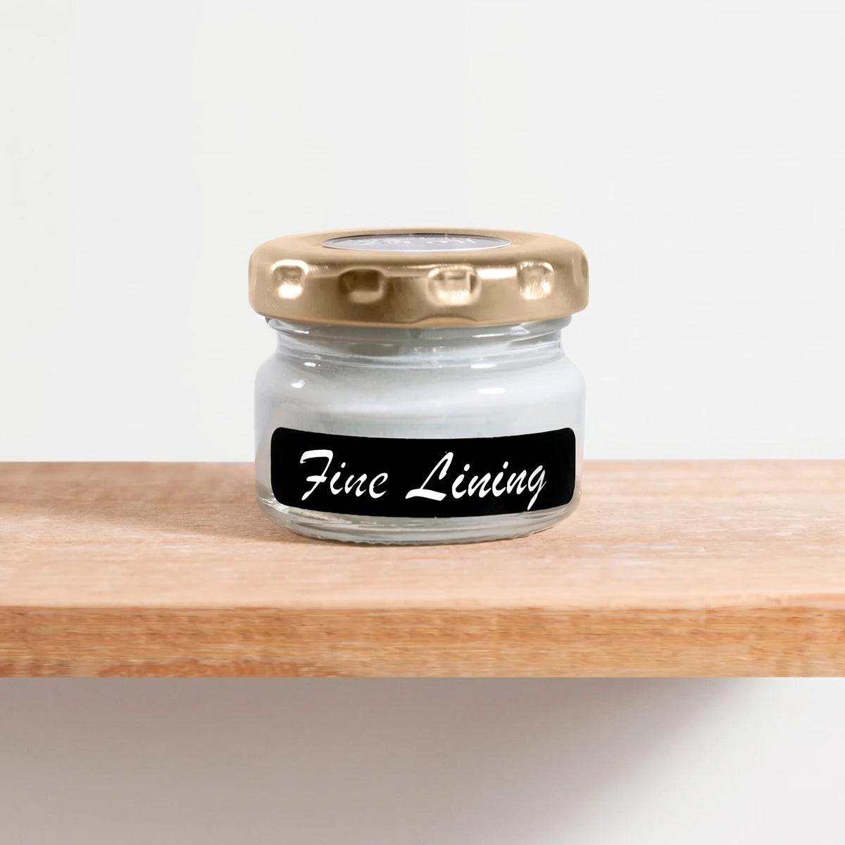 Small glass jar of Fine Lining 25ml chalk paint with a gold lid and black label, sitting on a wooden shelf.