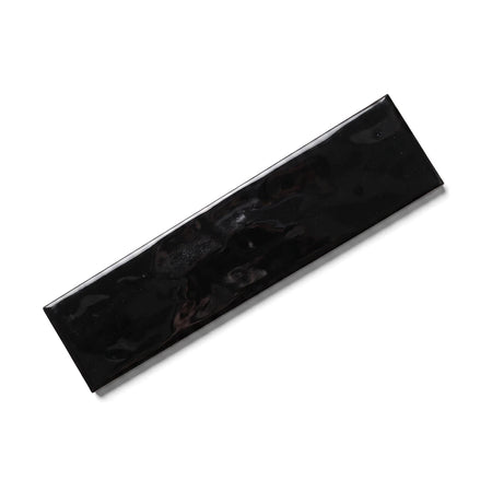 A single, rectangular, glossy black glazed subway tile, measuring 75x300mm, shown angled on a surface.