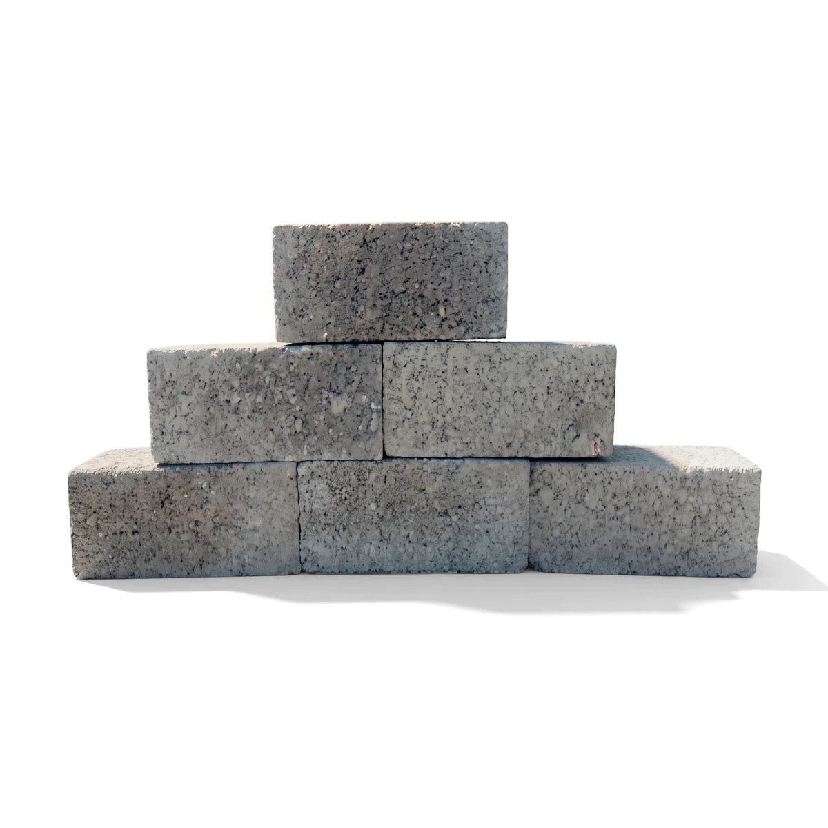 Stack of grey cement maxi bricks with a rough texture, arranged in a pyramid shape for construction.