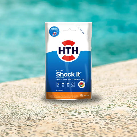HTH pool care pouch labeled Shock It in blue and white standing on a sandy poolside