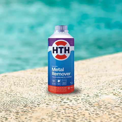 HTH pool care metal remover bottle standing on a pebble surface by blue water.