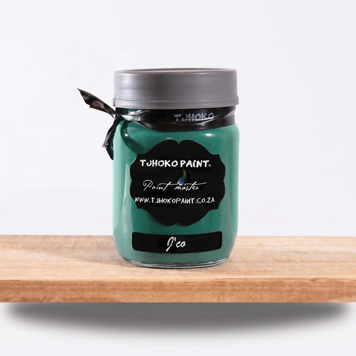J'Co 250ml Tjohoko Paint master chalk paint in a teal color glass jar with a dark lid and ribbon, sitting on a wooden shelf.
