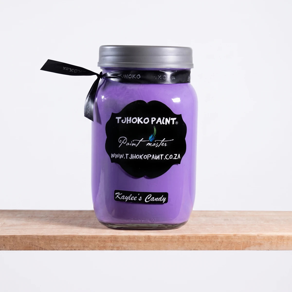 Kaylee's Candy 500ml Tjhoko purple chalk paint jar with a silver lid, black label, and ribbon, on a natural wooden shelf.