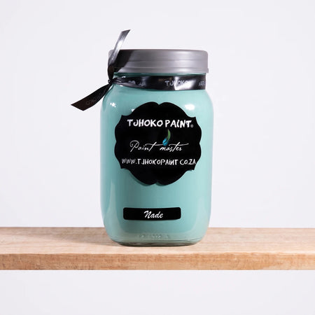A glass jar of TJ Hoko Paint in Nade, a light teal chalk paint, with a black label, displayed on a wooden shelf.