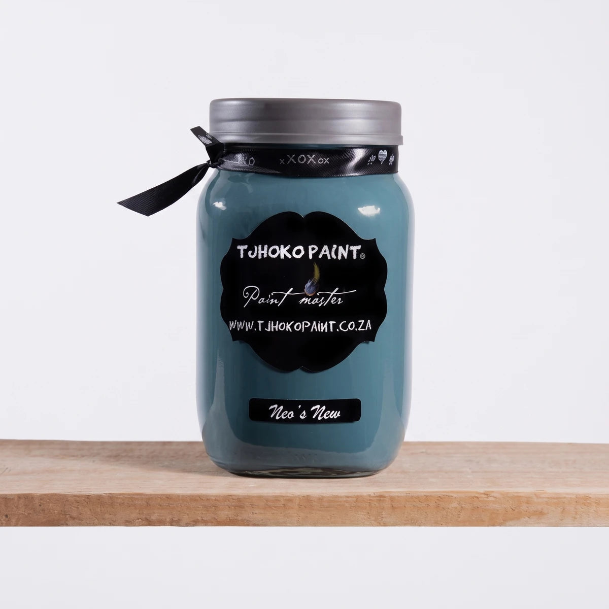 A Neo's New 1L Tjhoko teal chalk paint jar with a black label sits on a wooden shelf against a dark wall.