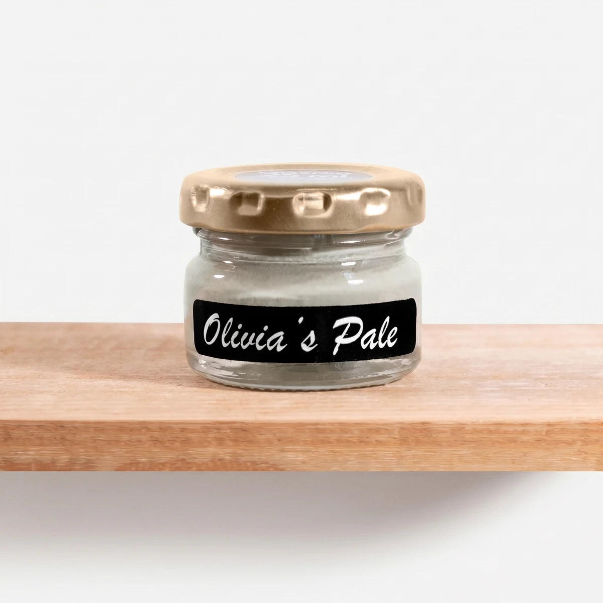 Small glass jar of Olivia's Pale 25ml Chalk Paint with a gold lid and black label, resting on a wooden shelf.