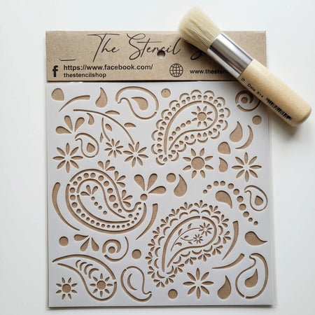 White paint stencil with intricate paisley and floral patterns, packaged and displayed flat alongside a round stencil brush.