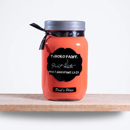 A glass jar of Paul's Place 1L Tjohoko Chalk Paint in a vibrant reddish-orange color with a black label, sitting on a light
