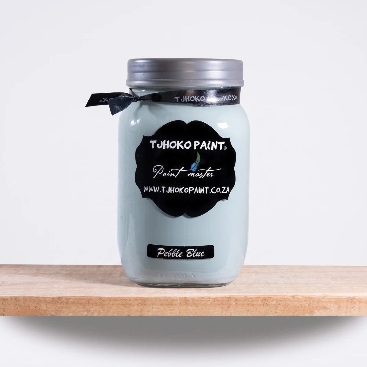 Pebble Blue 1L Chalk Paint in a clear glass jar with a silver lid, black ribbon, and label, displayed on a wooden shelf.