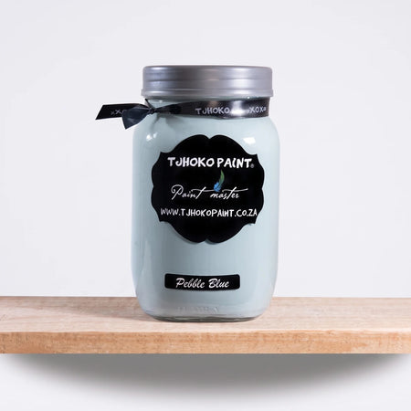 Pebble Blue 1L Chalk Paint in a clear glass jar with a silver lid, black ribbon, and label, displayed on a wooden shelf.