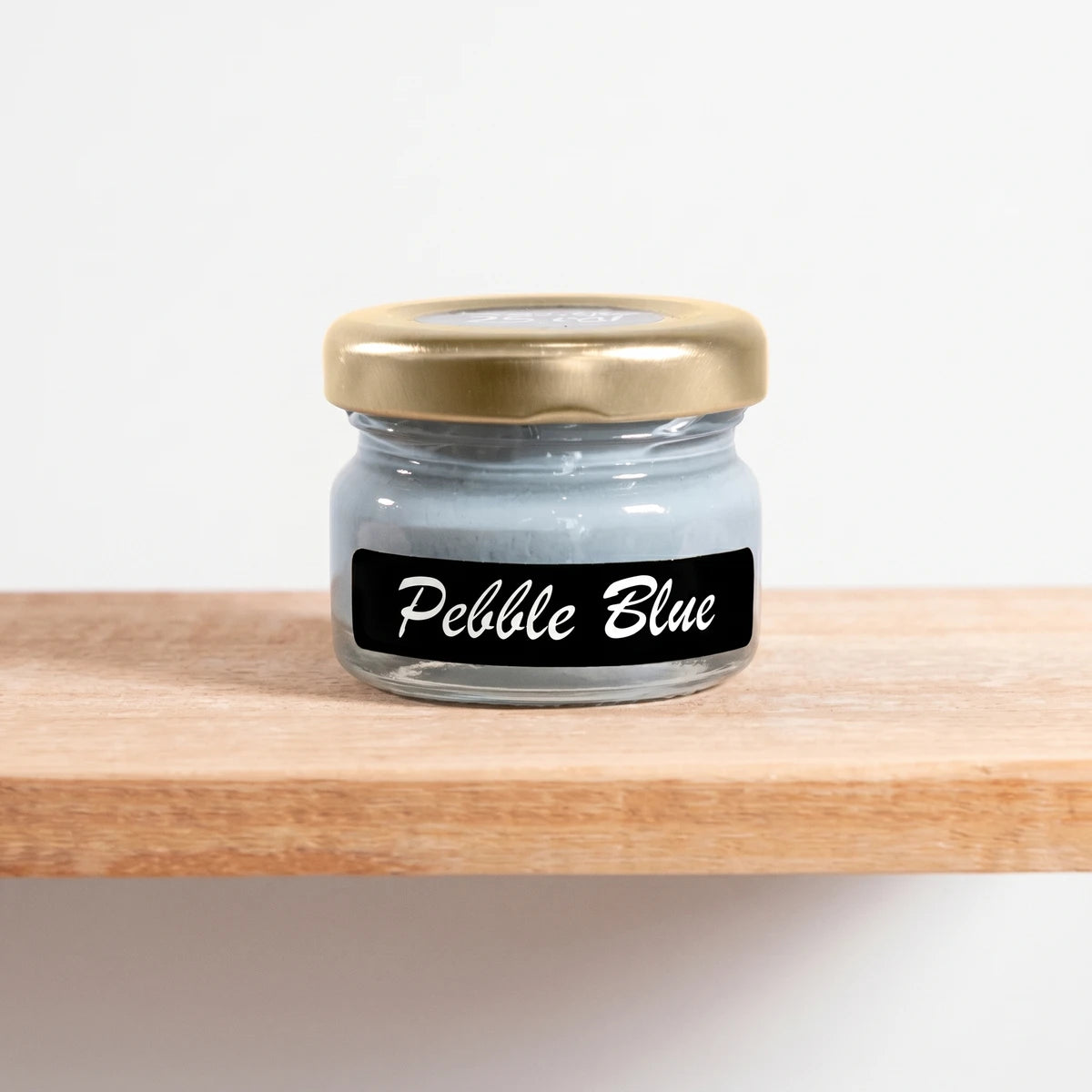 Pebble Blue 25ml chalk paint in a clear glass jar with a gold lid, sitting on a light wooden shelf.