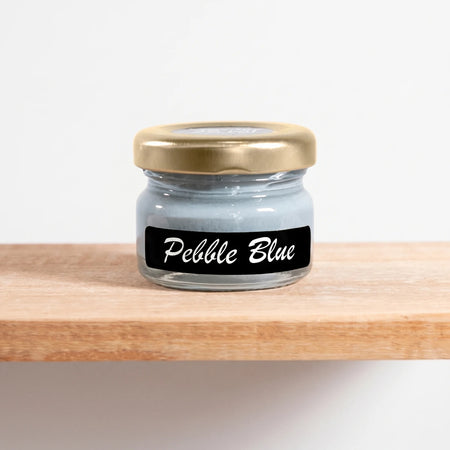 Pebble Blue 25ml chalk paint in a clear glass jar with a gold lid, sitting on a light wooden shelf.