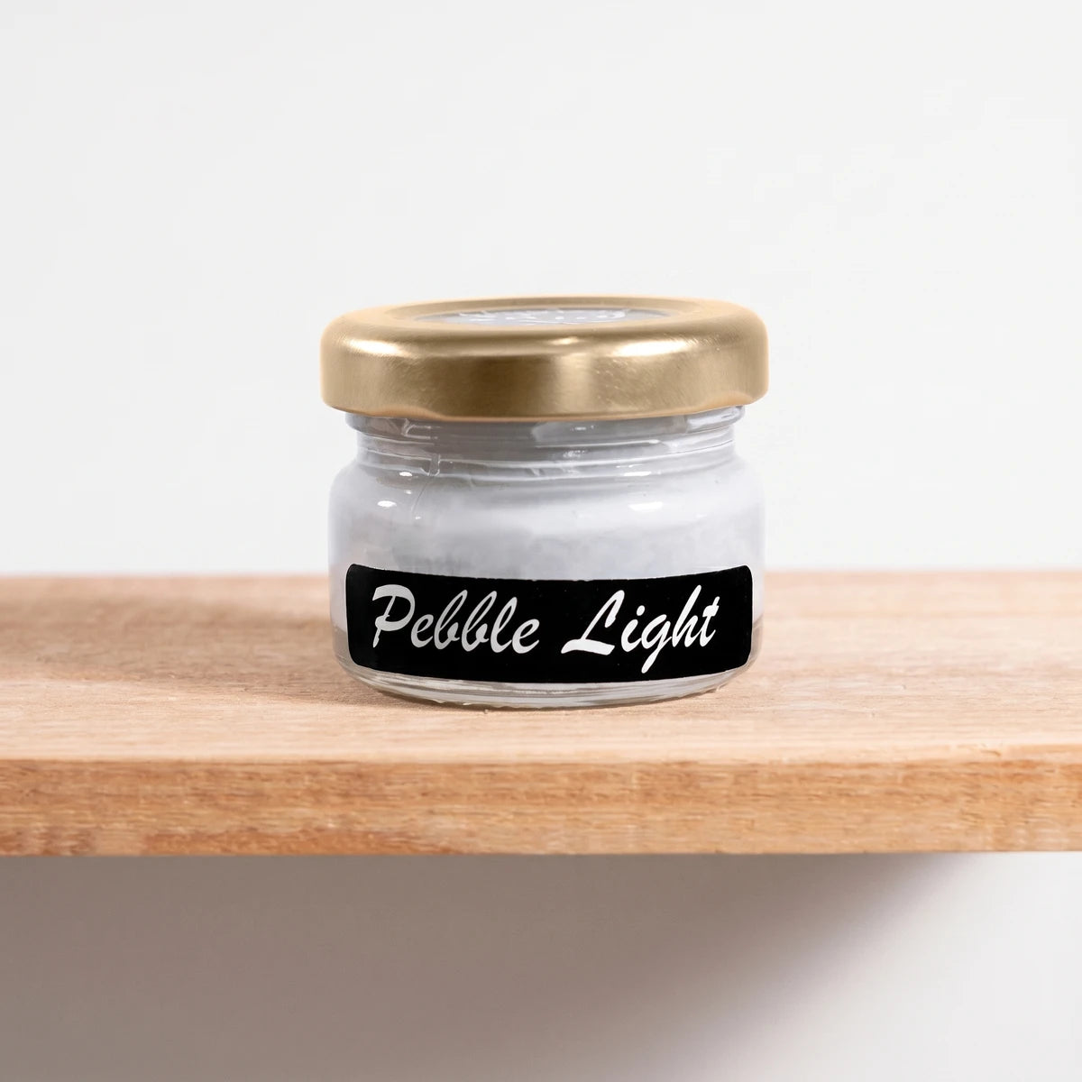 Pebble Light 25ml Chalk Paint in a small glass jar with a gold lid and black label on a wooden shelf.
