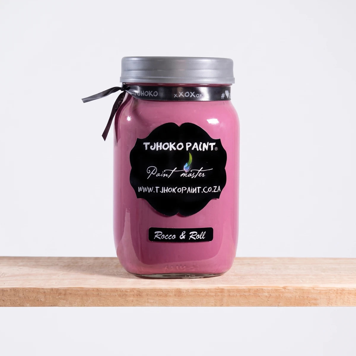 Rocco and Roll 1L Tjhoko Paint in a clear glass jar with a silver lid, filled with pink chalk paint, resting on a wooden