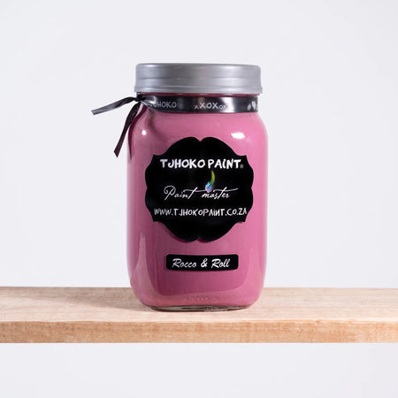 Rocco and Roll 1L Tjhoko Paint in a clear glass jar with a silver lid, filled with pink chalk paint, resting on a wooden