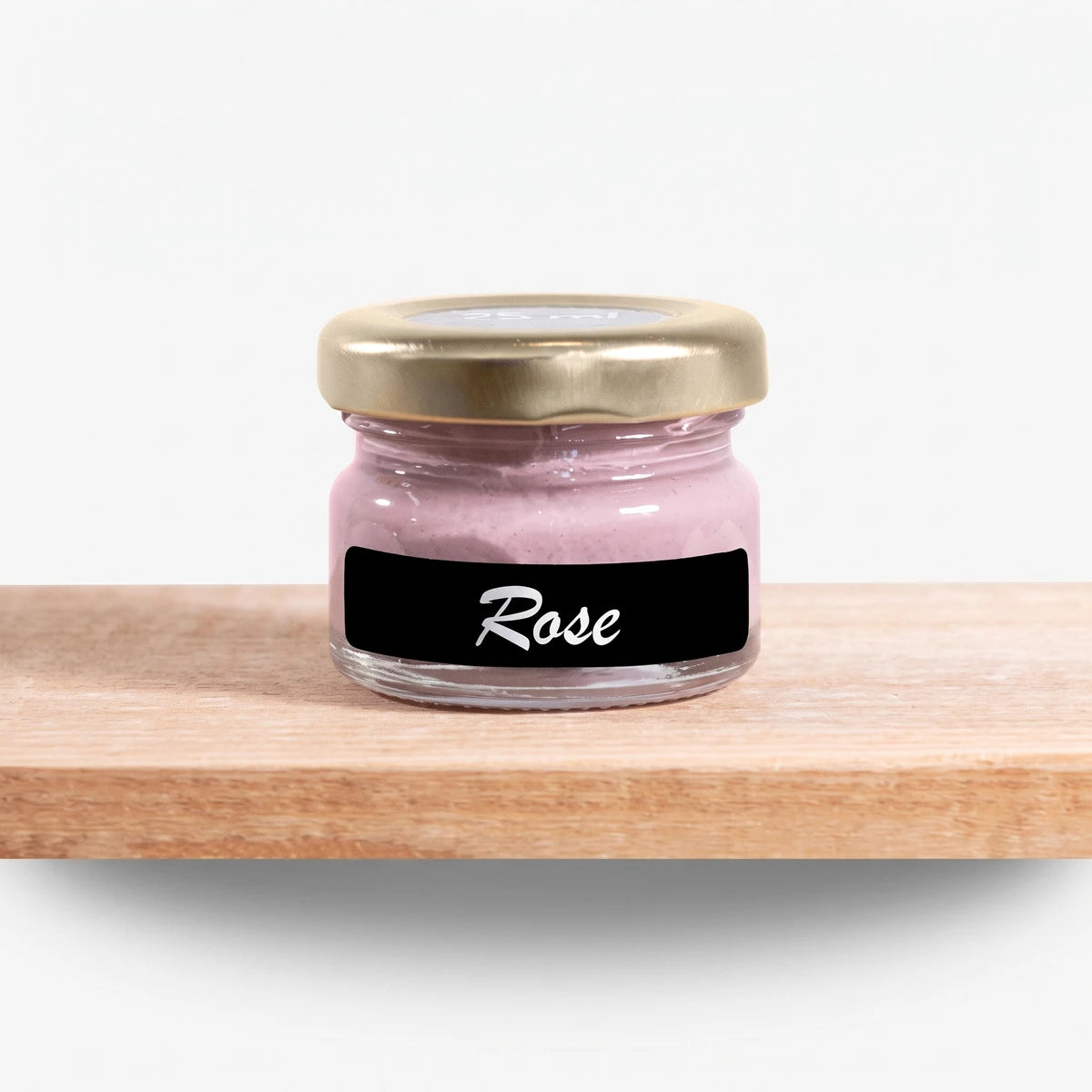 A small clear glass jar filled with rose pink chalk paint, featuring a gold lid and a black label with 'Rose' written in