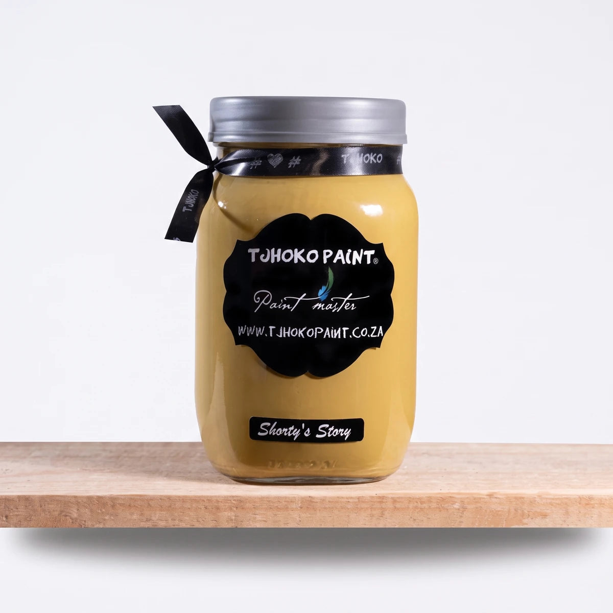 Shorty's Story 1Litre Chalk Paint in a yellow-gold glass jar with a black label and silver lid, resting on a wooden surface.