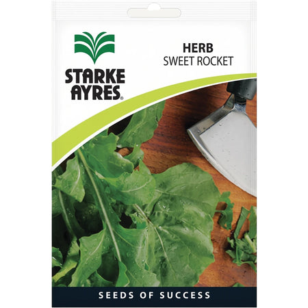 Starke Ayres Herb Sweet Rocket seed packet with fresh green rocket leaves and a small silver gardening tool on a wooden