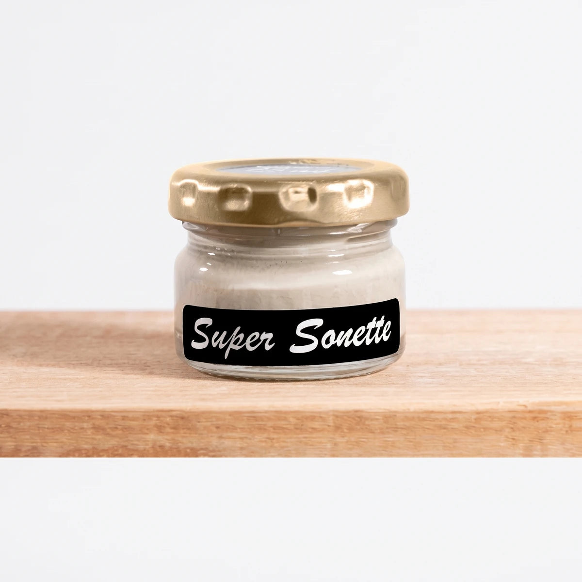Small clear glass jar of Super Sonette 25ml chalk paint with a gold lid and black label, displayed on a light wooden shelf.
