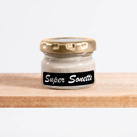 Small clear glass jar of Super Sonette 25ml chalk paint with a gold lid and black label, displayed on a light wooden shelf.