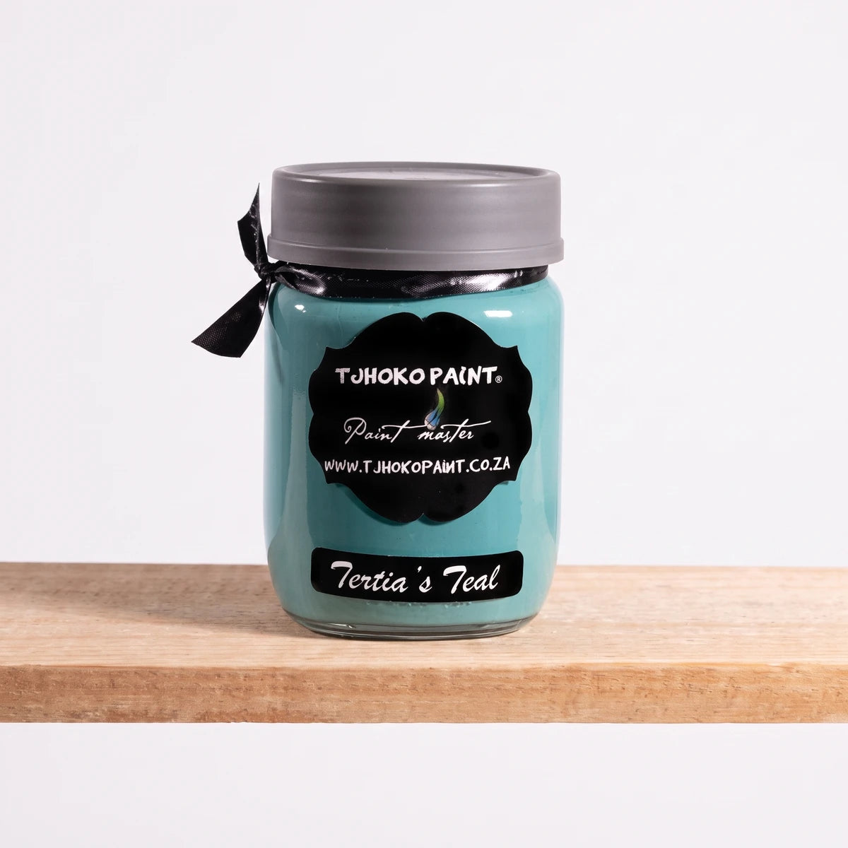 Tertia's Teal 250ml chalk paint in a clear glass jar with a black label and gray lid, sitting on a wooden shelf.