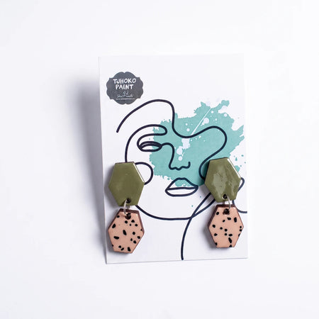 Pair of Tjhoko Chrystal's Art hexagonal drop earrings with glossy olive green and speckled peach sections on a display card.