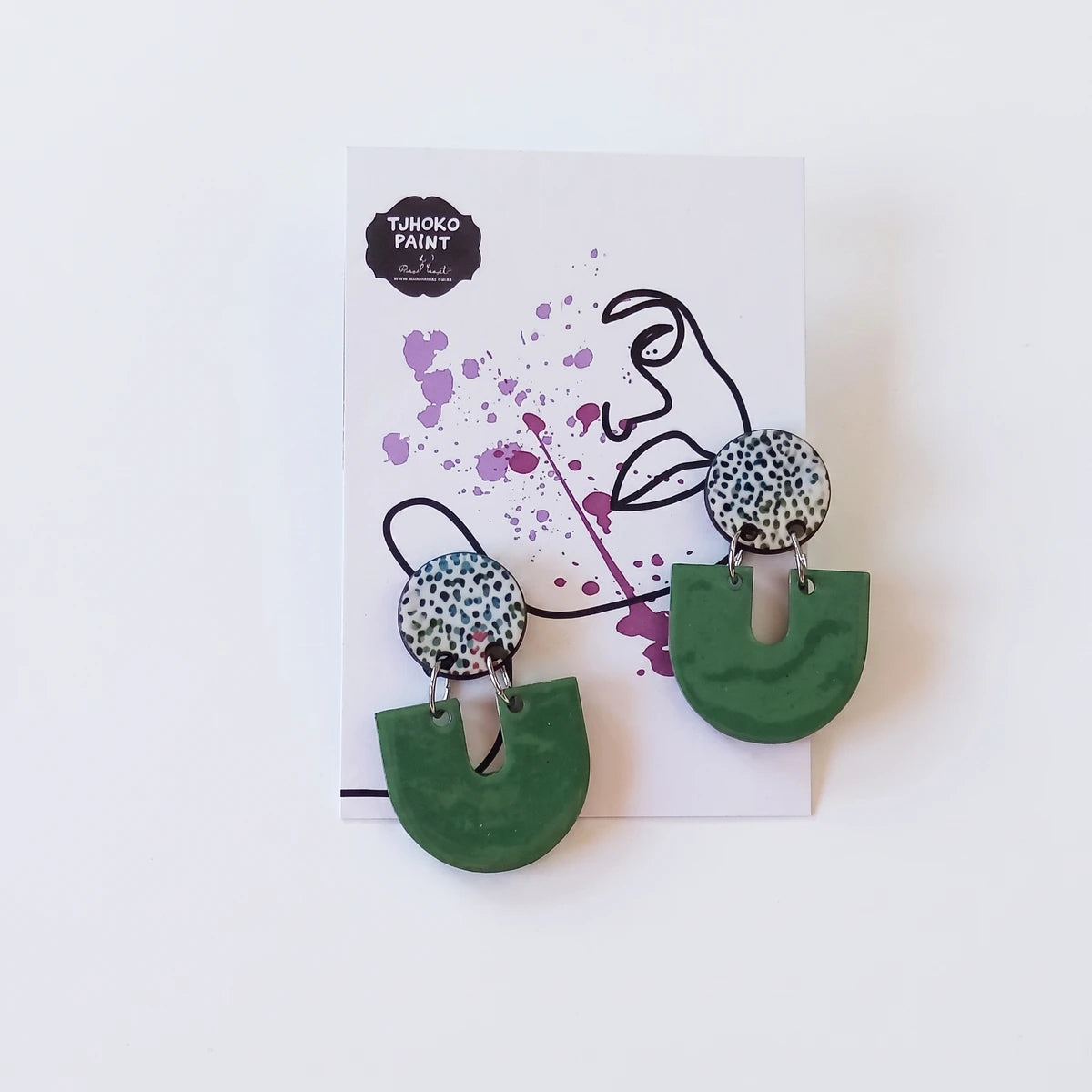 A pair of Tjhoko Dumisa's Dots earrings featuring speckled white and green circular studs with dark green U-shaped pendants,