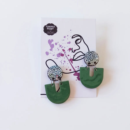 A pair of Tjhoko Dumisa's Dots earrings featuring speckled white and green circular studs with dark green U-shaped pendants,