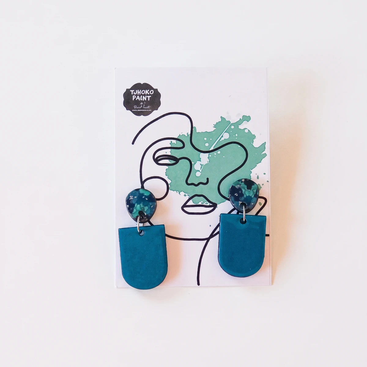 A pair of Tjhoko Jane's Flowers blue polymer clay dangle earrings with speckled studs on a white display card.