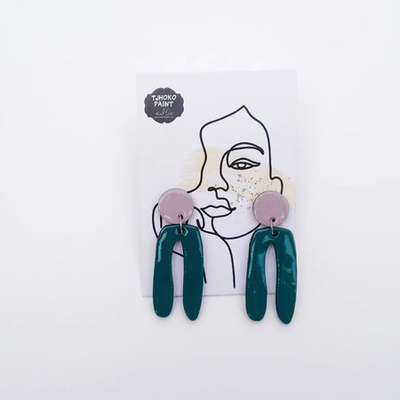 Pair of Tjhoko J'Co Painted Bellies dangle earrings featuring dark teal U-shaped drops and pale pink studs, presented on a