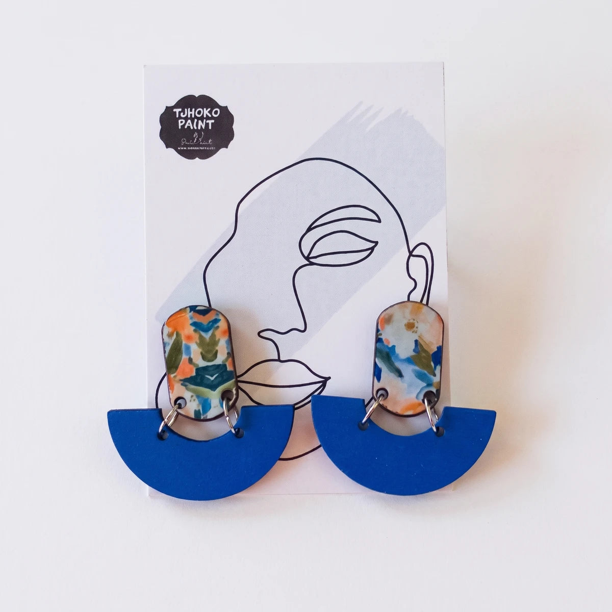 A pair of Tjhoko Paint Bob's Blue Painted Art Earrings with abstract colorful designs and royal blue semi-circles, displayed