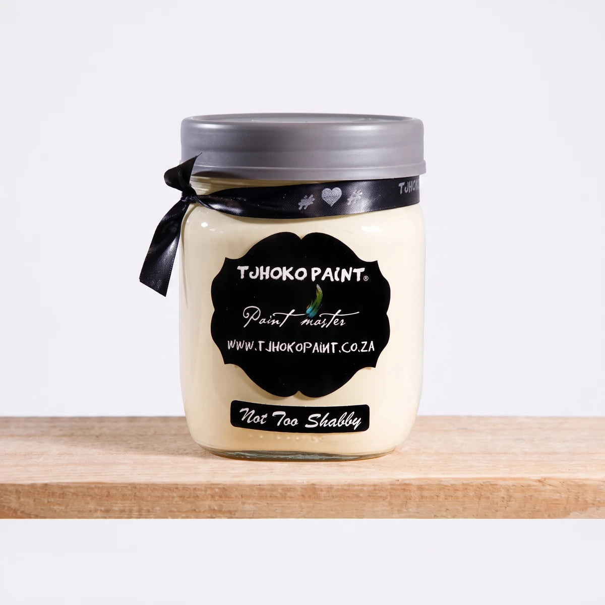 Tjhoko Paint 'Not Too Shabby' 500ml chalk paint jar with a grey lid, black ribbon, and black label, sitting on a wooden
